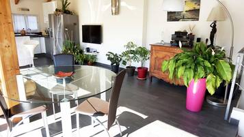 Une cuisine moderne dotée d’un réfrigérateur encastré, d’un coin repas avec une table et des chaises en verre, et d’un meuble en bois agrémenté d’objets décoratifs.