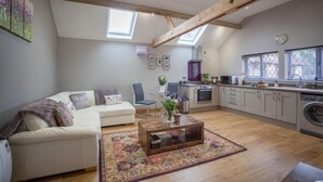 A spacious living area with a sofa, a coffee table, and a rug. There is a kitchen with a washing machine and a dining area with a chair. - Little Oak (Hereford)