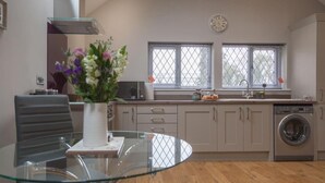 A modern kitchen with a glass dining table, a microwave, a washing machine, and a clock on the wall. - Little Oak (Hereford)