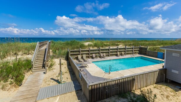 Eine Holzterrasse führt zu einem Poolbereich mit Liegestühlen und Blick auf das Meer.