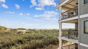 Ein zweistöckiges Gebäude mit einem Balkon mit Blick auf einen Strand mit Dünen und Vegetation.