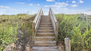 Eine Holztreppe führt zu einer Holzplattform, umgeben von hohem Gras und Vegetation.