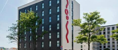 A modern hotel building with a prominent red logo on the side.