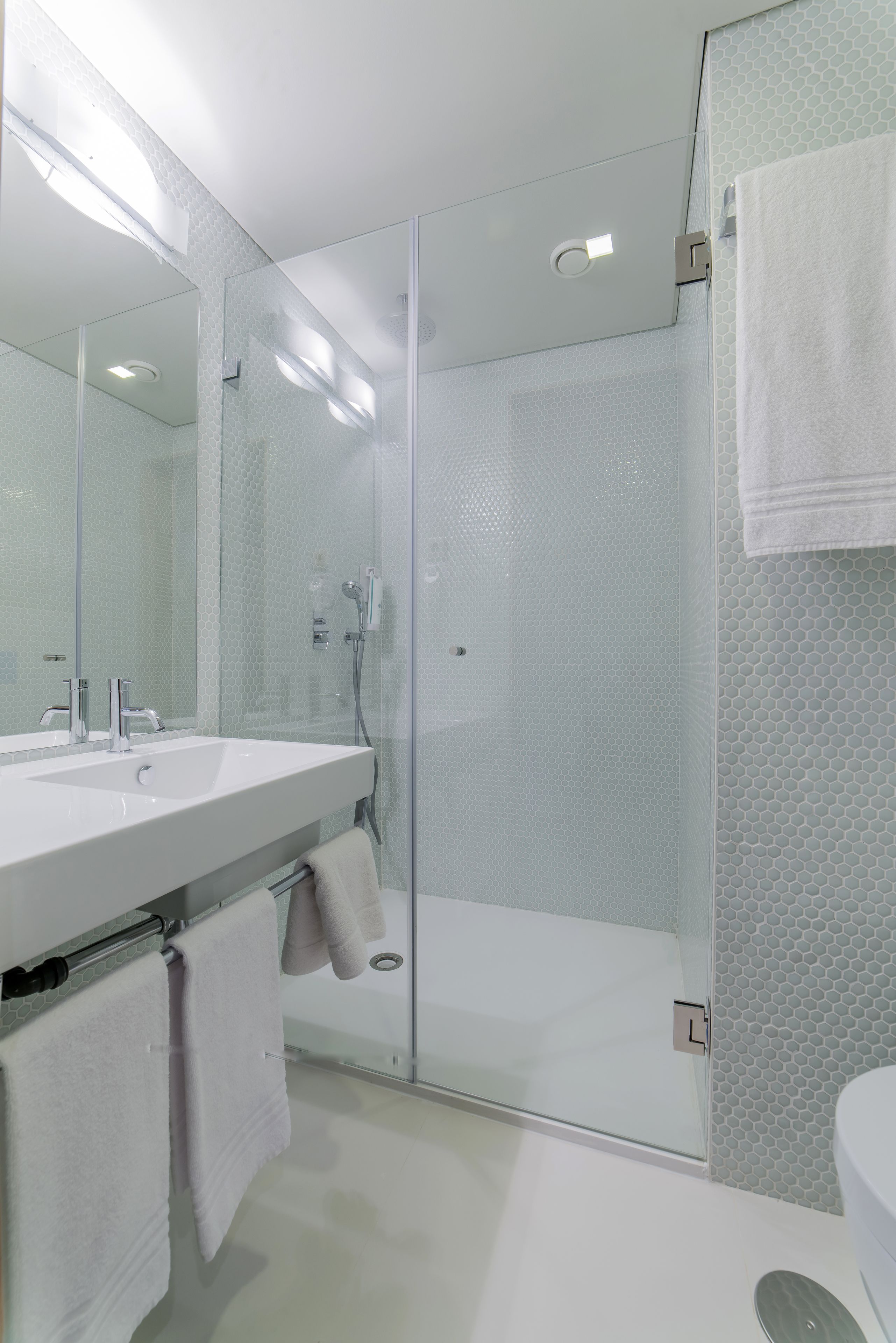 A modern bathroom with a glass-enclosed shower, a large mirror, and a white sink.