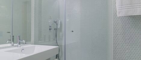A modern bathroom with a glass-enclosed shower, a large mirror, and a white sink.