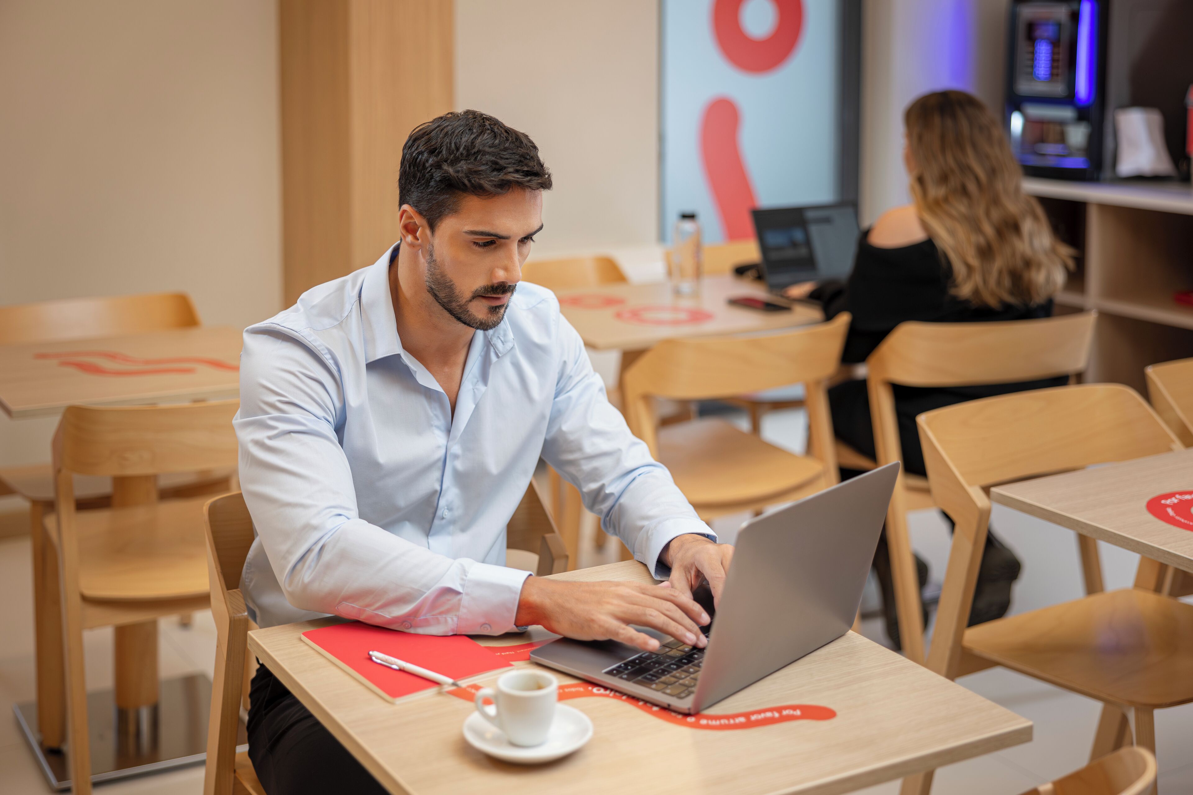A man working on a laptop in a modern office setting with wooden furniture and a casual atmosphere.