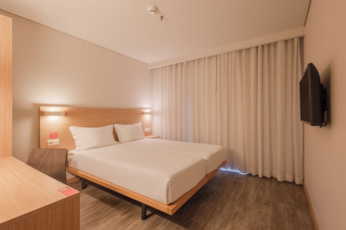 A hotel room with a wooden bed, a desk, a flat-screen TV, and a large window with curtains.