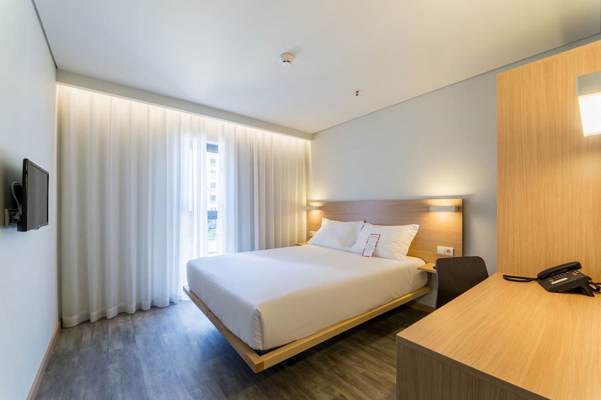 A hotel room with a bed, a desk, a phone, and a TV.