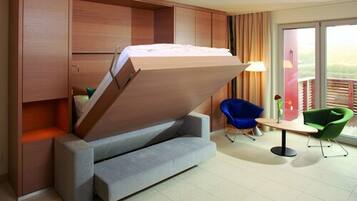 A compact room with a foldable bed, a small table, a blue chair, and a green chair.