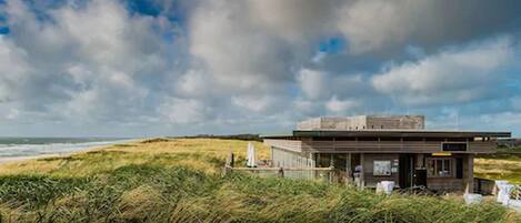 Een modern strandhuis met een plat dak, gelegen op een grasachtige duin met uitzicht op de oceaan.