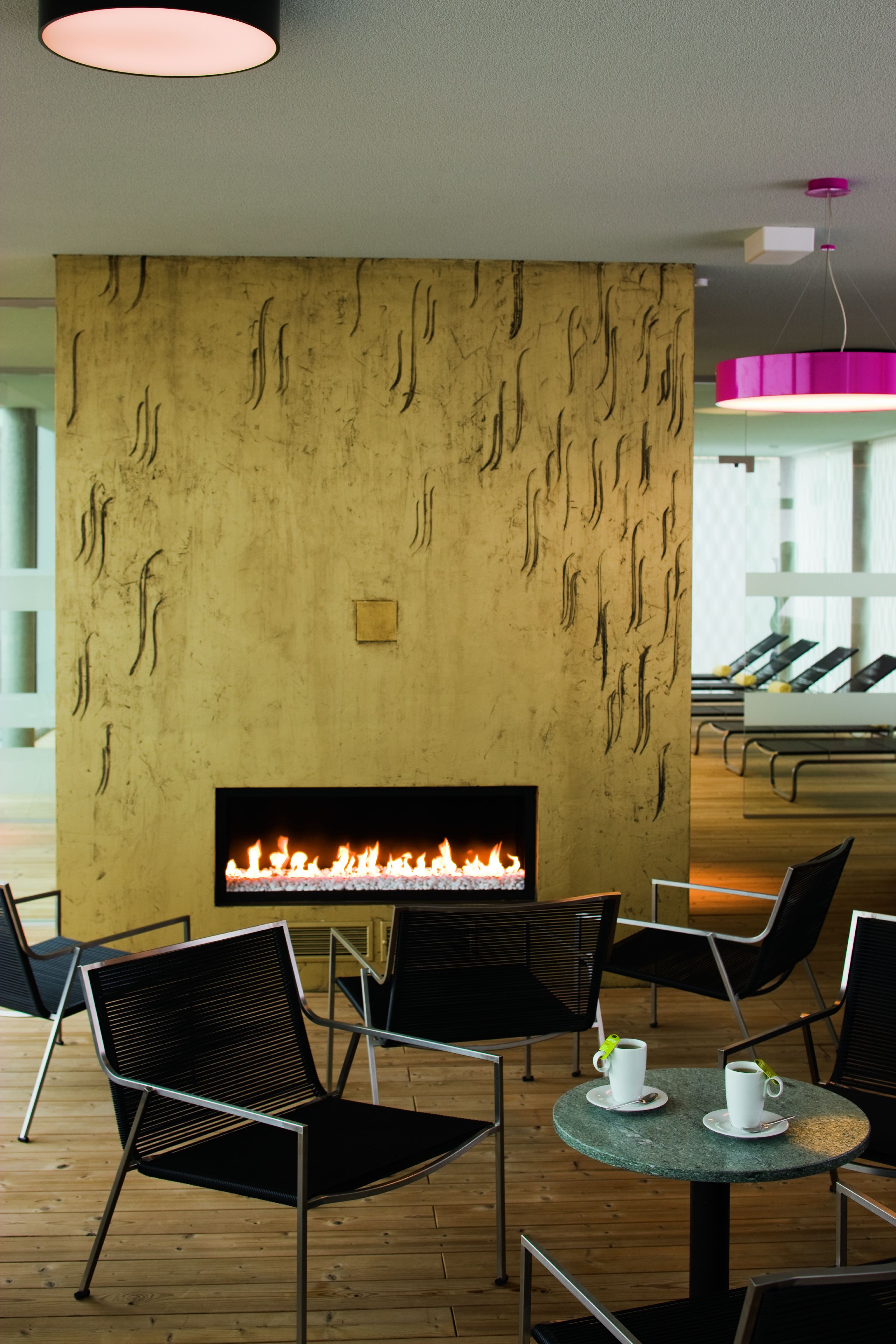 A modern lounge area with a fireplace, black chairs, and a round table with cups.