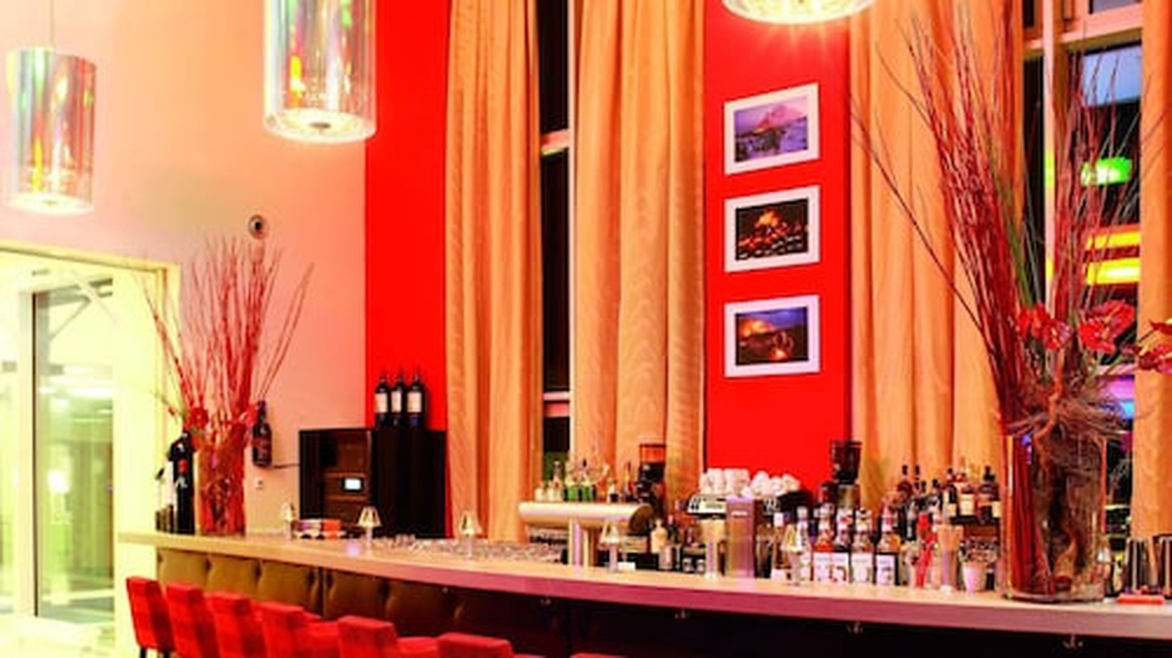 A bar area with red walls, a long counter, and multiple bottles of alcohol.