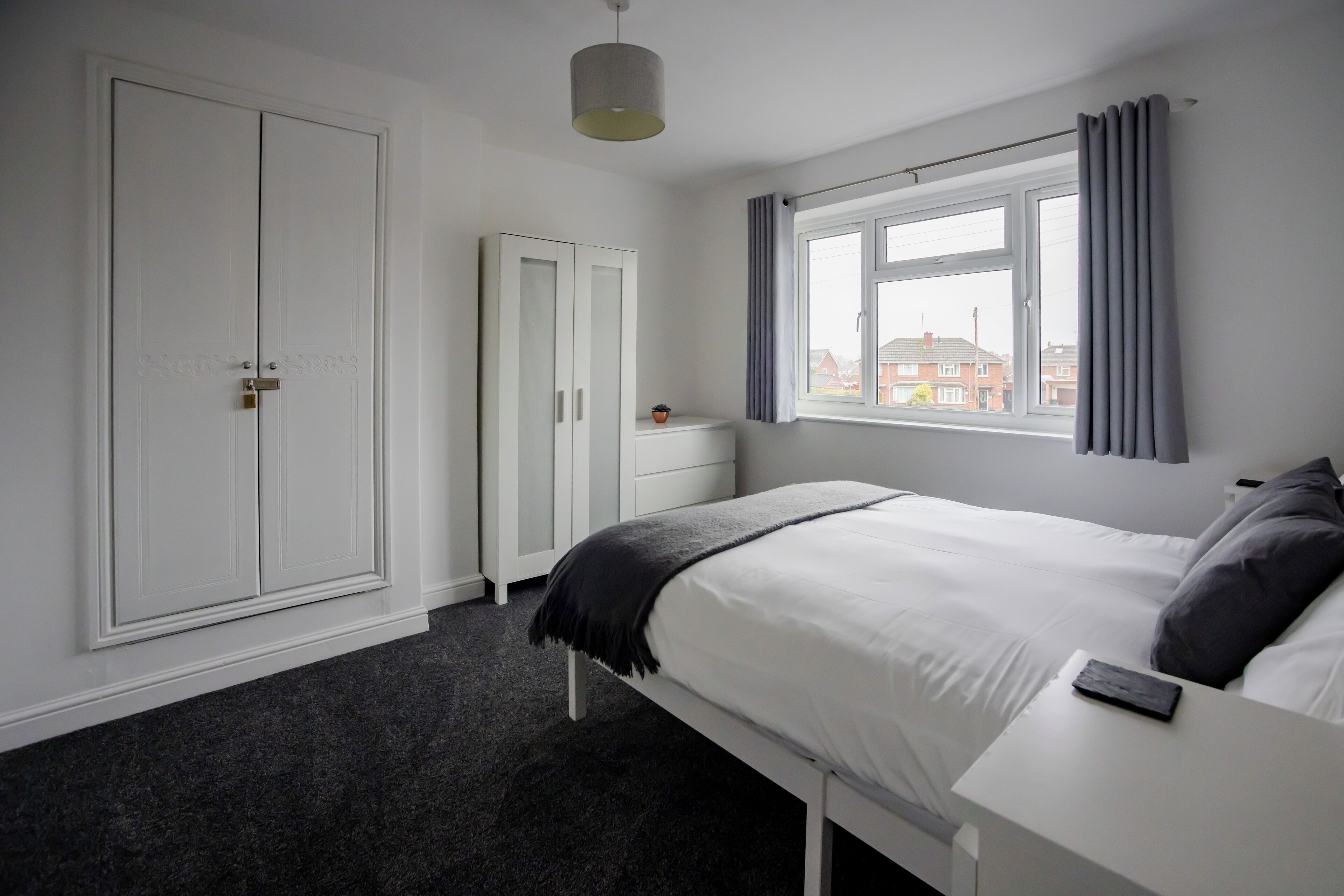 A bedroom with a bed, a nightstand, a wardrobe, and a window with curtains.