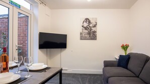 A modern living room with a flat-screen TV, a gray sofa, and a dining table set for two. - Raven House (Hereford)