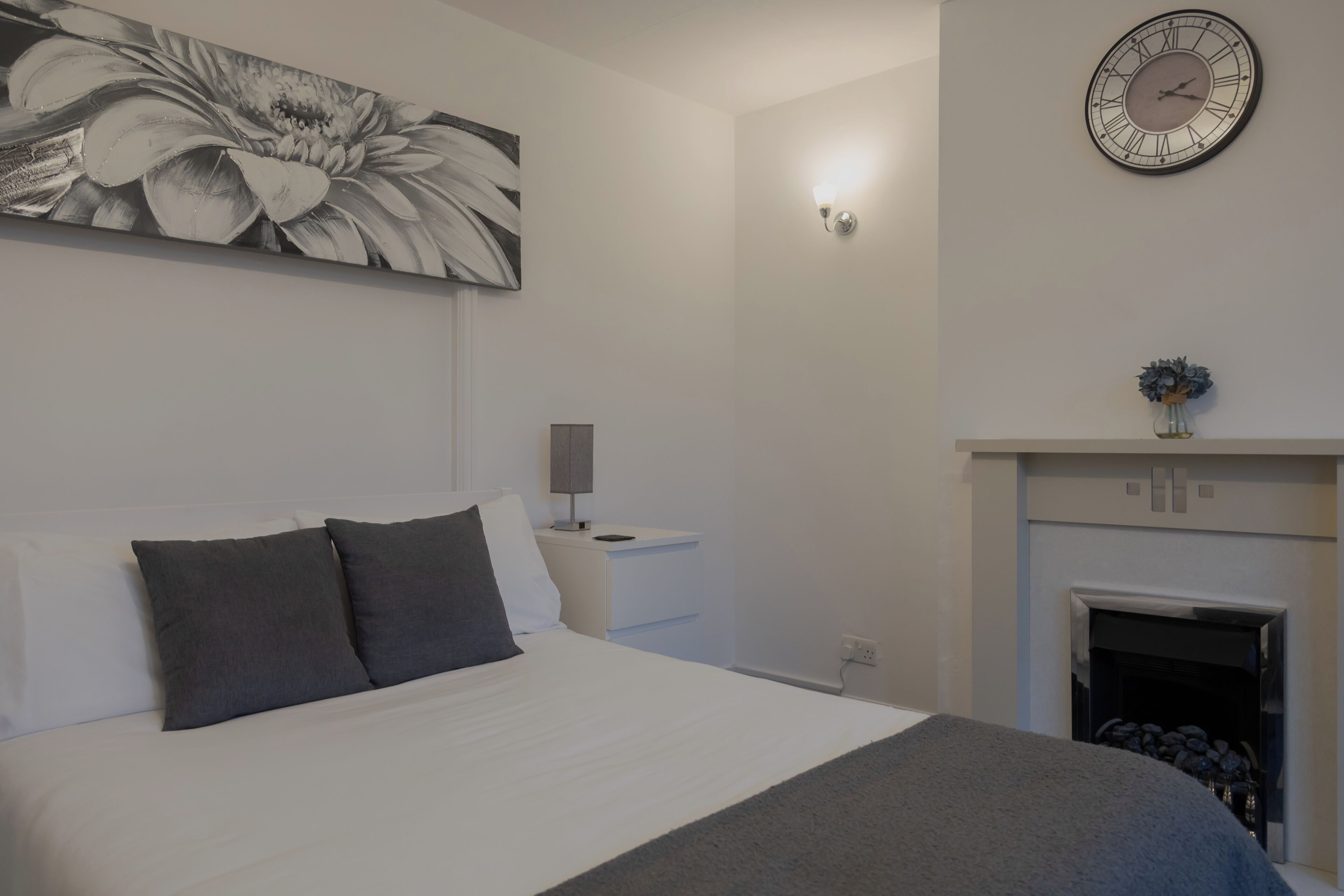 A bedroom with a bed, a nightstand, a wall clock, and a fireplace.