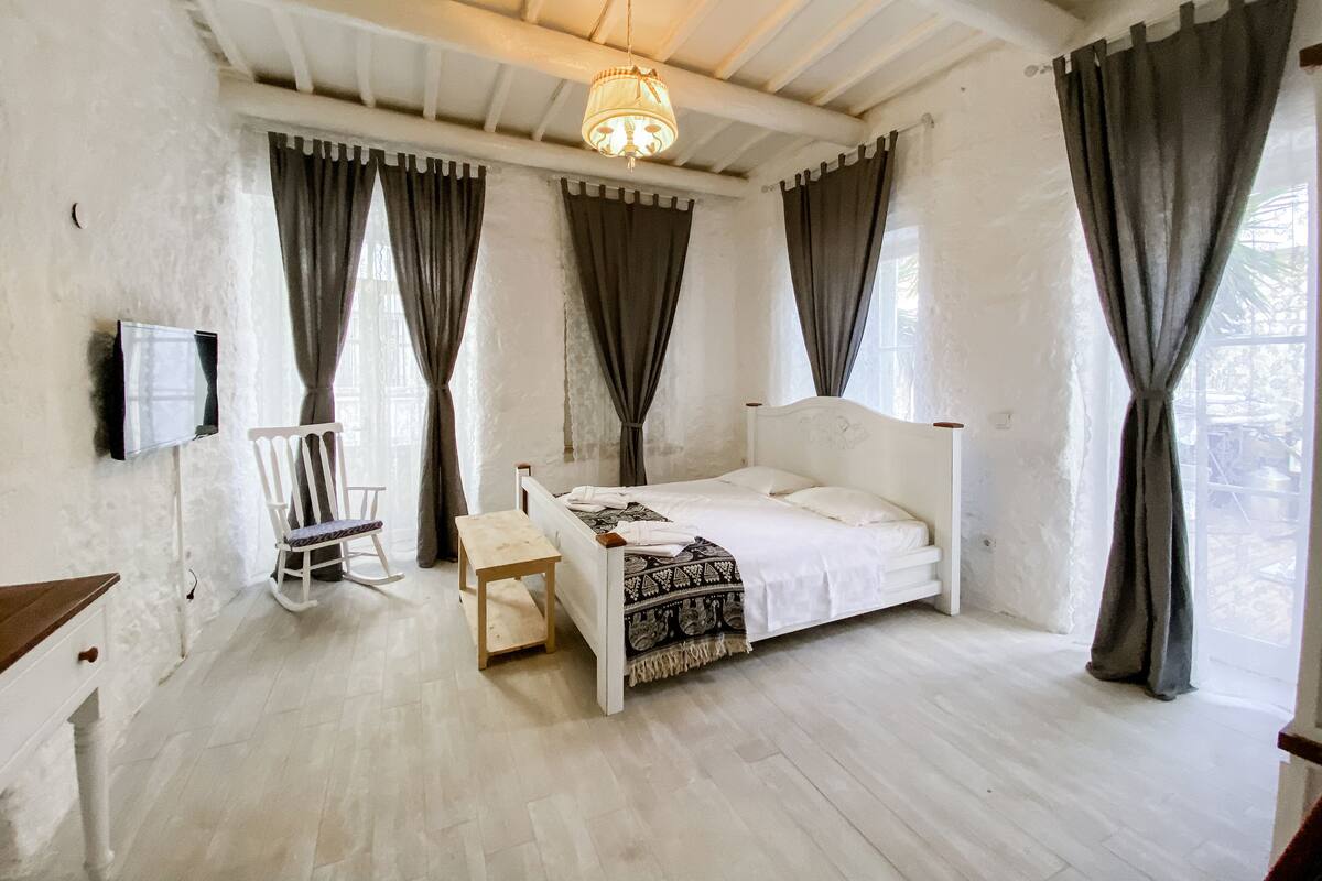 A bedroom with a bed, a desk, a chair, and a hanging light fixture.