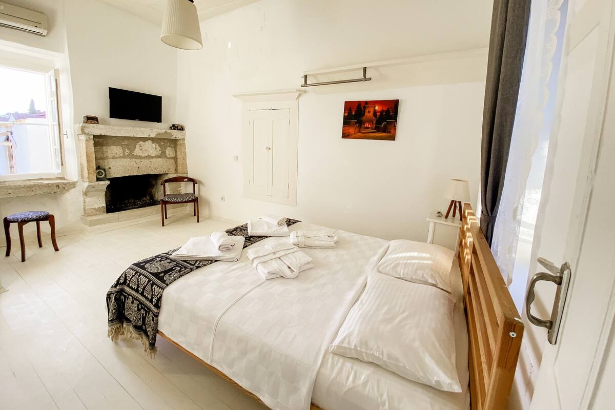 A bedroom with a bed, a television, a fireplace, a chair, and a window.