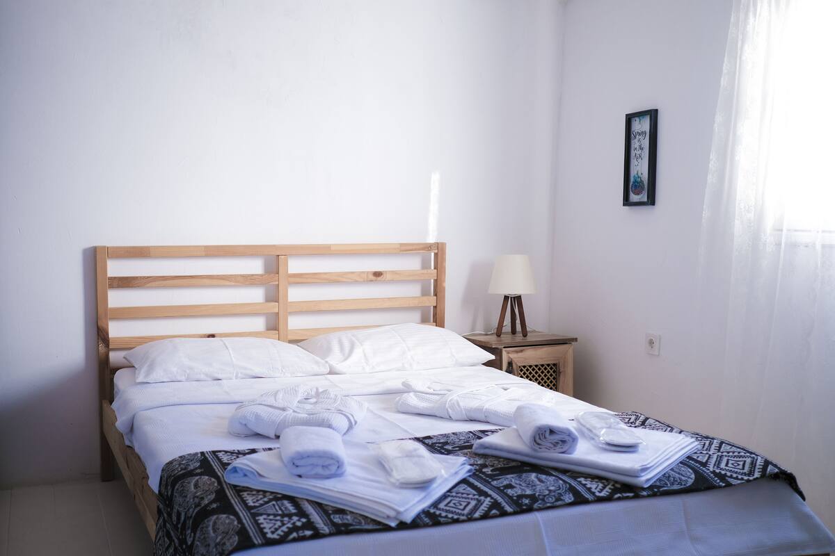 A neatly made bed with white linens and rolled towels, a bedside lamp, and a framed picture on the wall.