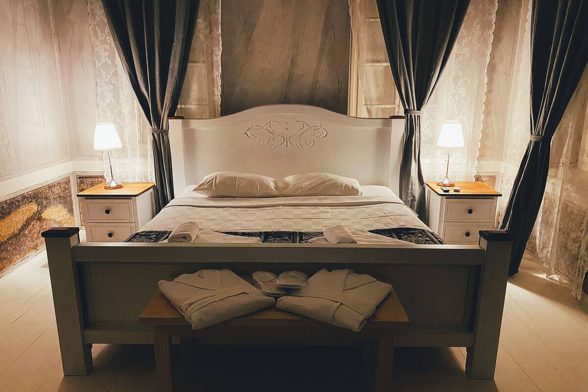 A neatly made bed with a headboard, two bedside tables with lamps, and a wooden bench at the foot of the bed.