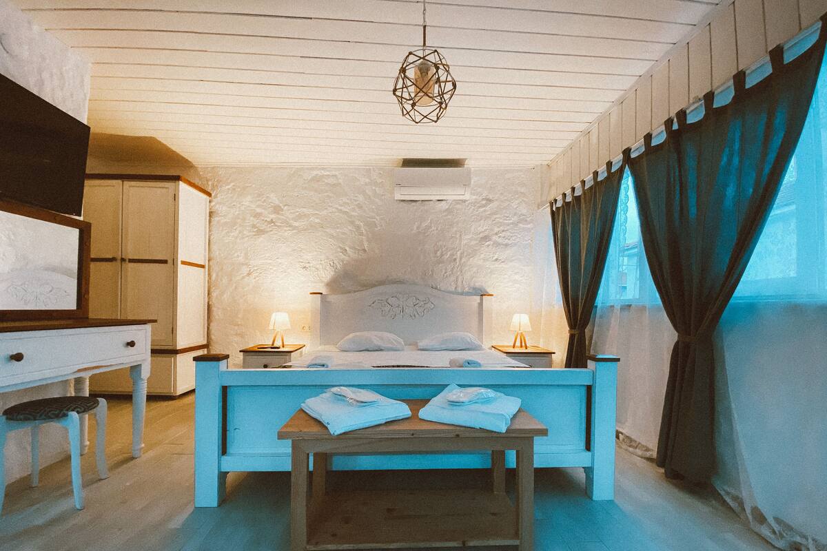 A bedroom with a bed, bedside tables, a desk, and a hanging light fixture.