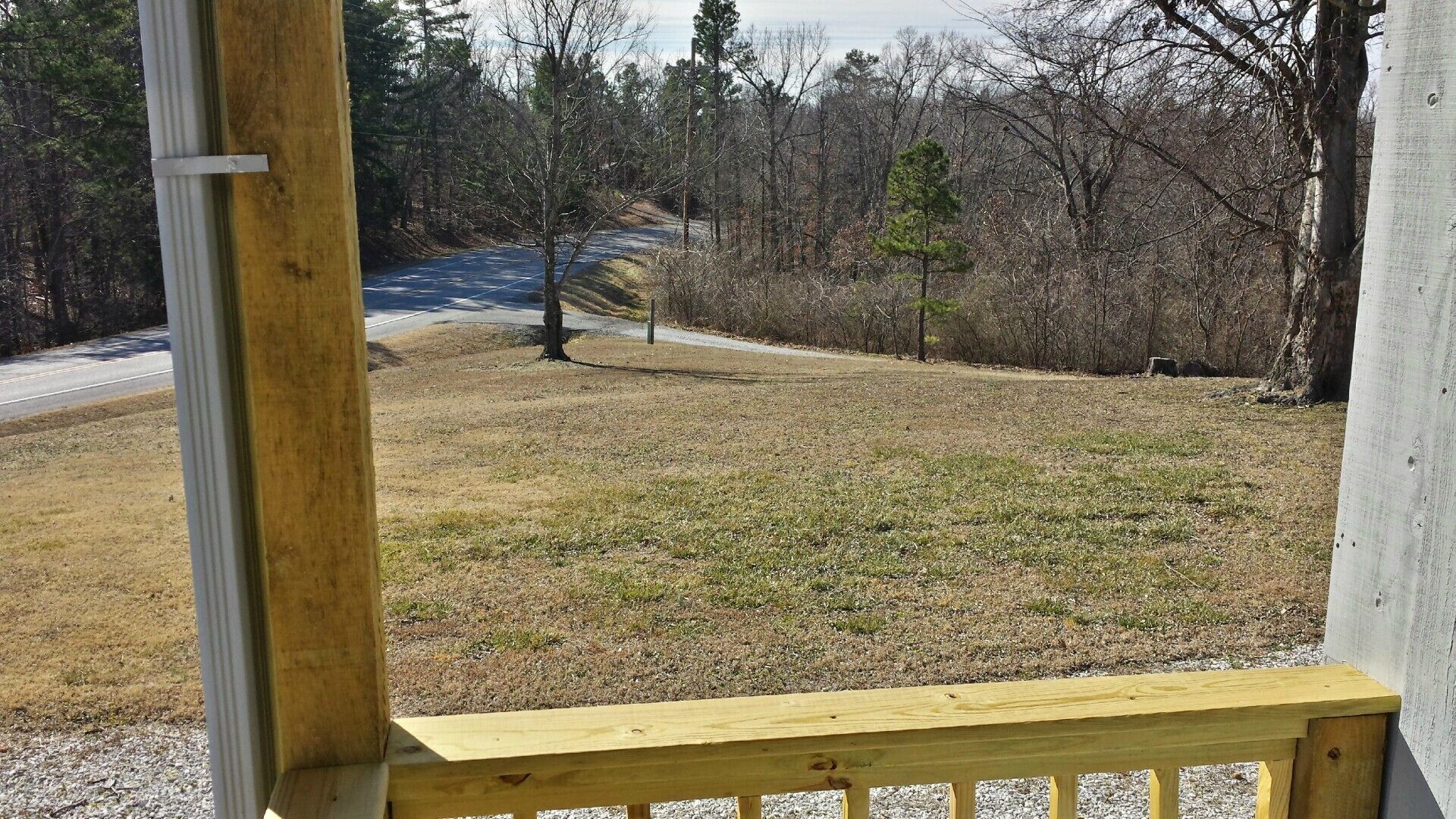 A view from a wooden deck overlooking a grassy area with a road in the distance.