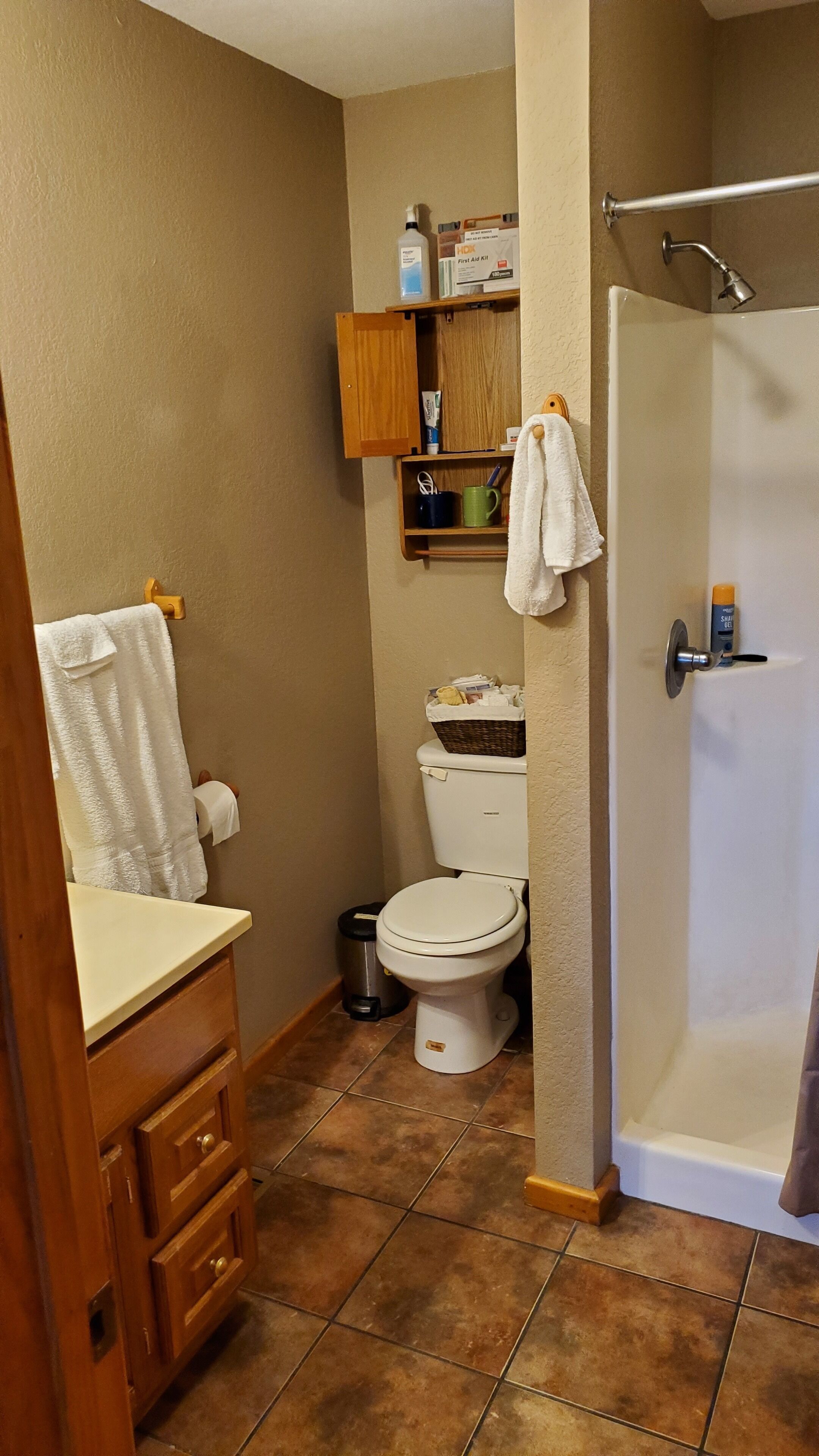 A bathroom with a toilet, sink, and shower. There is a cabinet above the toilet and a towel hanging on the wall.