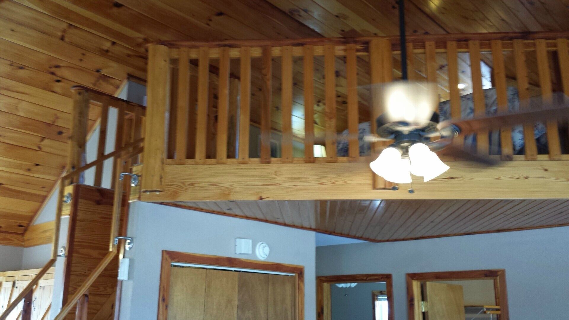 A room with a wooden ceiling, a ceiling fan, and a staircase leading to an upper level.