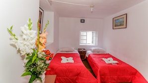 A room with two beds, a window, a painting, and a vase with flowers.