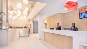 Ein moderner Empfangsbereich mit einem Holzbüro, einem digitalen Bildschirm und einer Treppe, die in eine obere Etage führt.