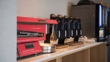 Una cocina comercial con un equipo rojo para hacer panqueques, una máquina de café y una exhibición de tazas de café negras.