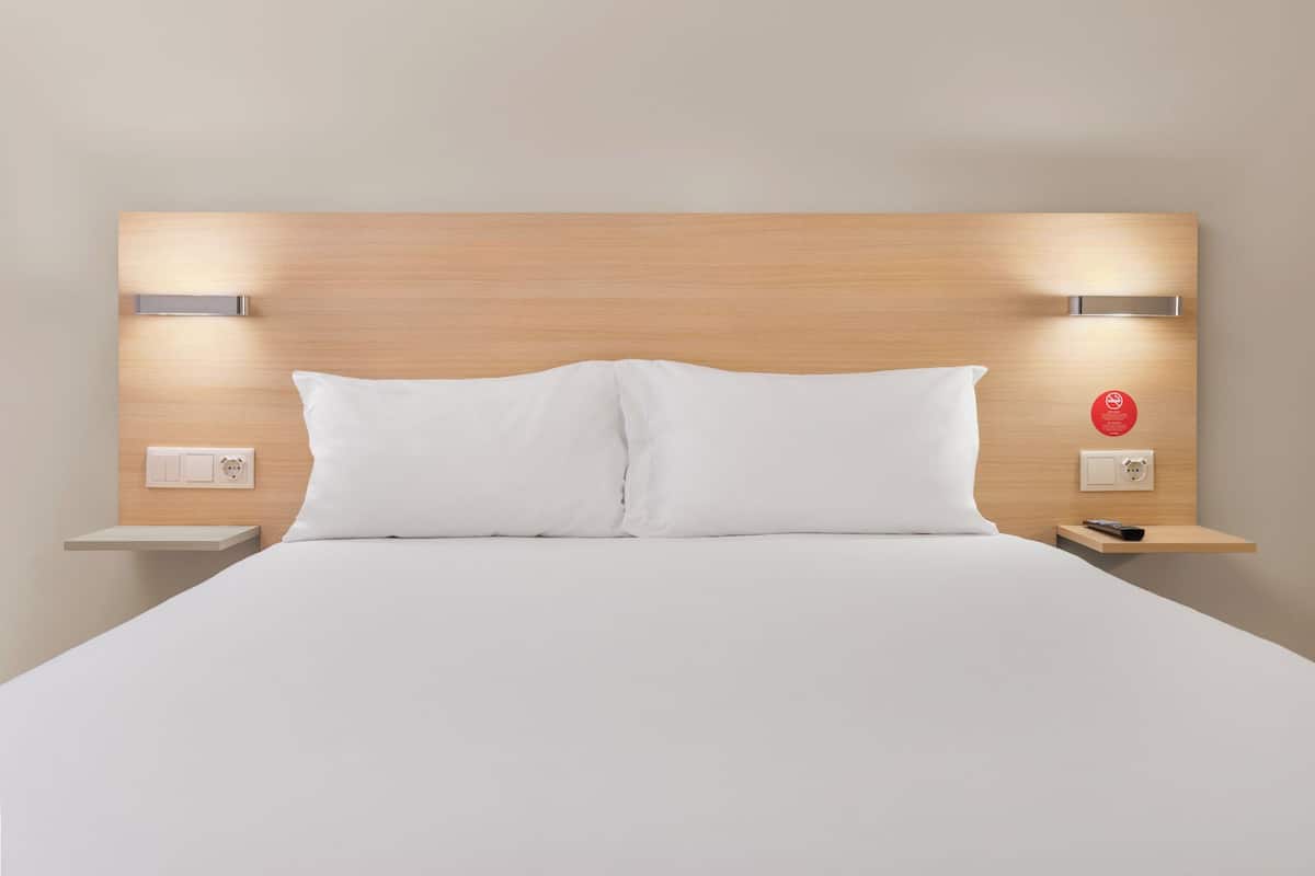 Ein Hotelzimmer mit einem hölzernen Kopfende, zwei Nachttischen, einem Bett mit weißer Bettwäsche und einem roten Schild an der Wand.