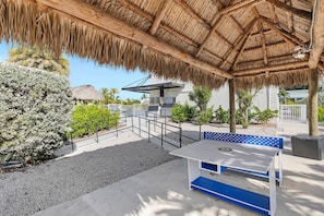 Un espacio al aire libre cubierto con techo de paja, una piscina y una estación de barbacoa.