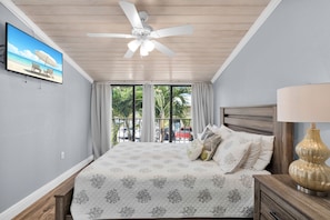 Une chambre avec un lit, un ventilateur de plafond, une télévision et une vue sur l’extérieur.