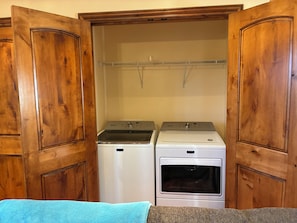 A laundry room with two washing machines and a dryer, enclosed by wooden doors. - Comfy Gathering Place for Friends or Family! (Montrose)