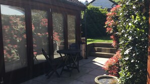 A patio with a table and chairs, a birdbath, and a view of a garden with red flowers. - Whortleberry Studio - delightful bright airy ensuite B&B (Porlock)