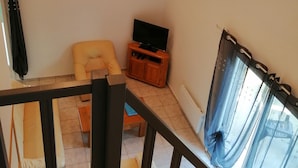 Ett rum med en soffa, en tv på ett träställ och ett fönster med gardiner.