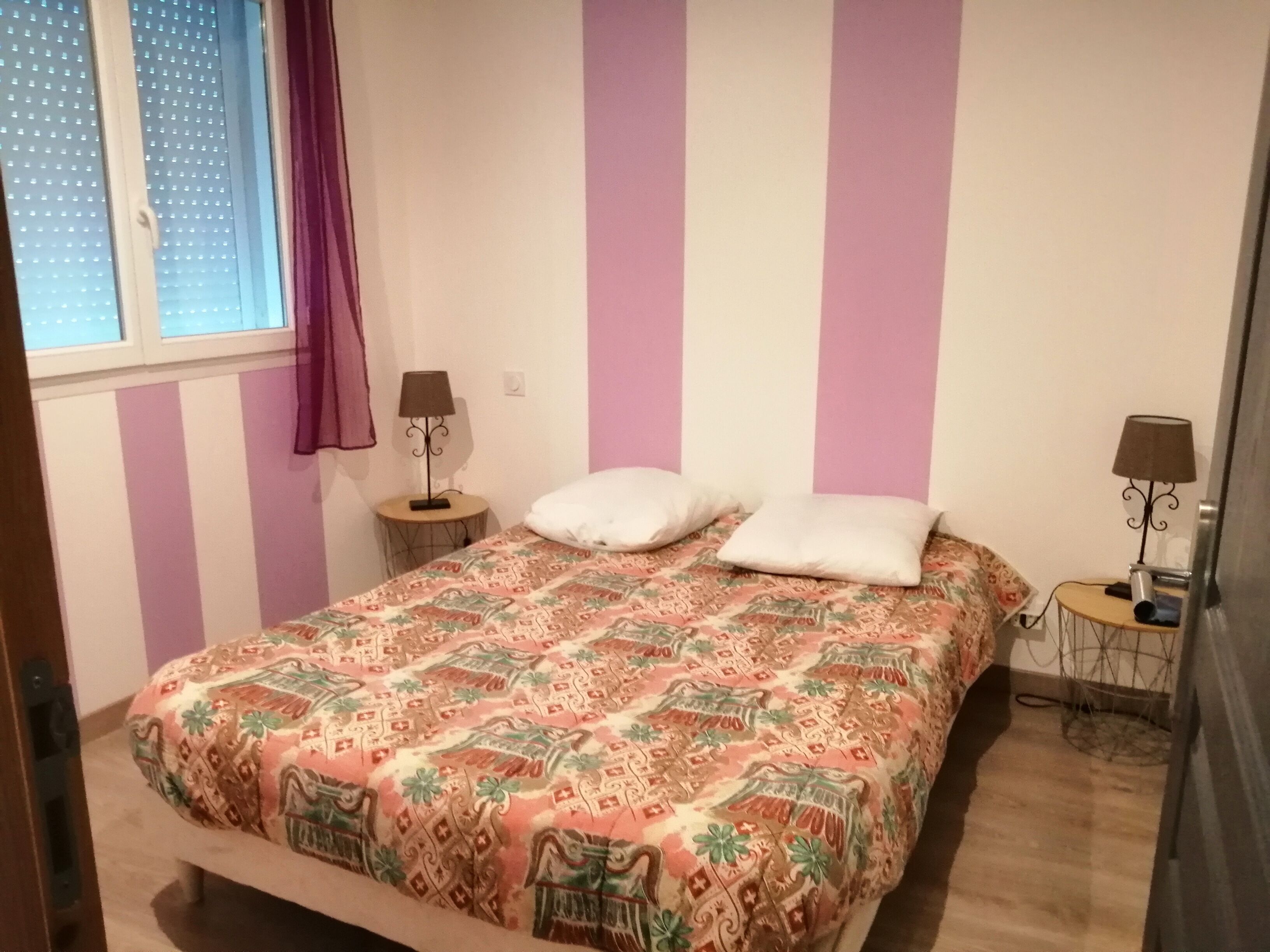 Un dormitorio con cama, dos mesitas de noche, una ventana con cortinas y una puerta.