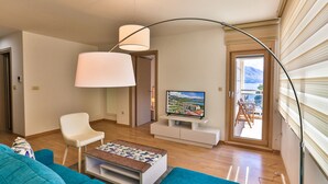 A modern living room with a sofa, a white armchair, a TV on a stand, and a large window with a view of the outdoors.