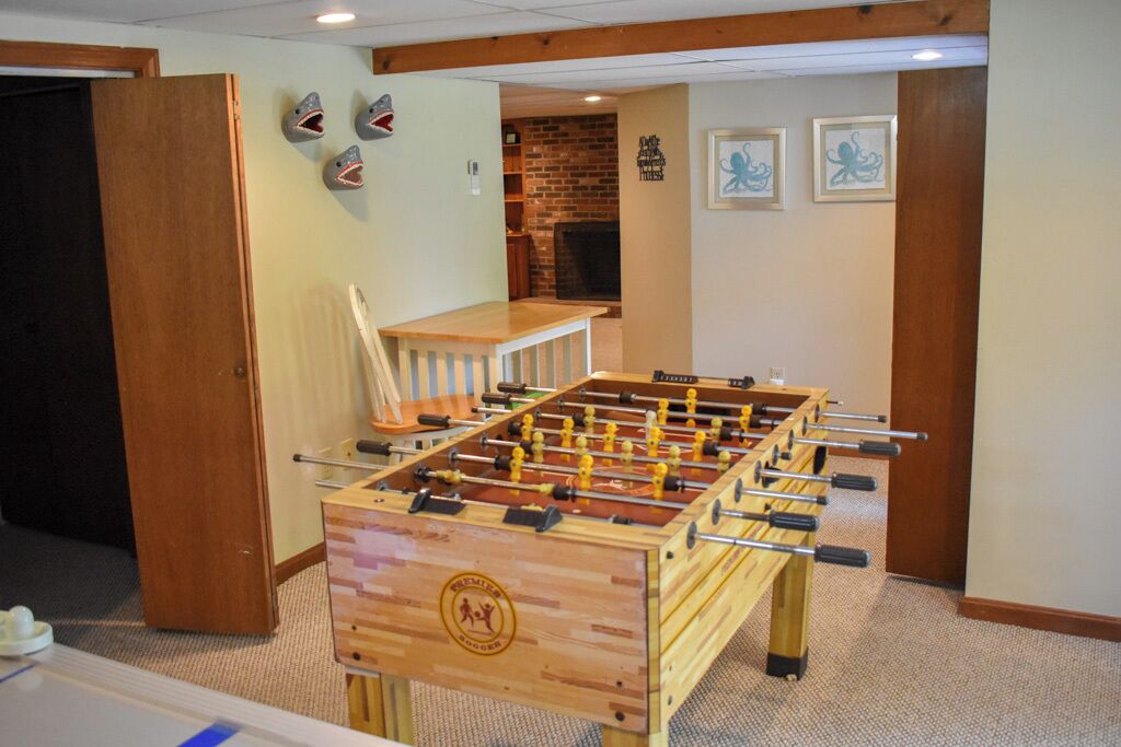 Een tafelvoetbaltafel in een kamer met een bakstenen muur, houten meubels en kunstwerken in lijsten aan de wanden.
