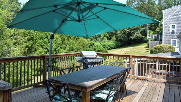 Eine Holzterrasse mit Tisch, Stühlen, einem Grill und einem grünen Sonnenschirm.
