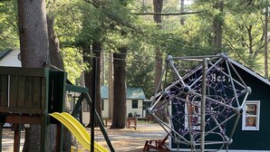 A playground with a yellow slide and a climbing structure, surrounded by trees and a picnic table.