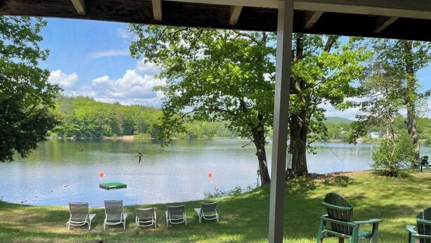 A lakeside view from a covered area with chairs and tables, trees, and a calm lake.