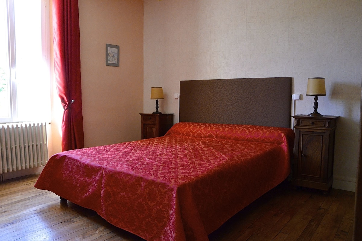 A room with a bed, two bedside tables with lamps, a radiator, and a window with curtains.