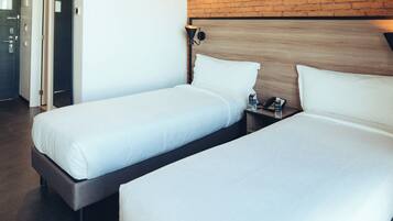 A hotel room with two single beds, a wooden headboard, a nightstand with a phone and a water bottle, and a brick wall.