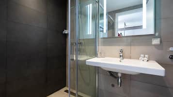 A modern bathroom with a glass shower enclosure, a white sink, and a large mirror.