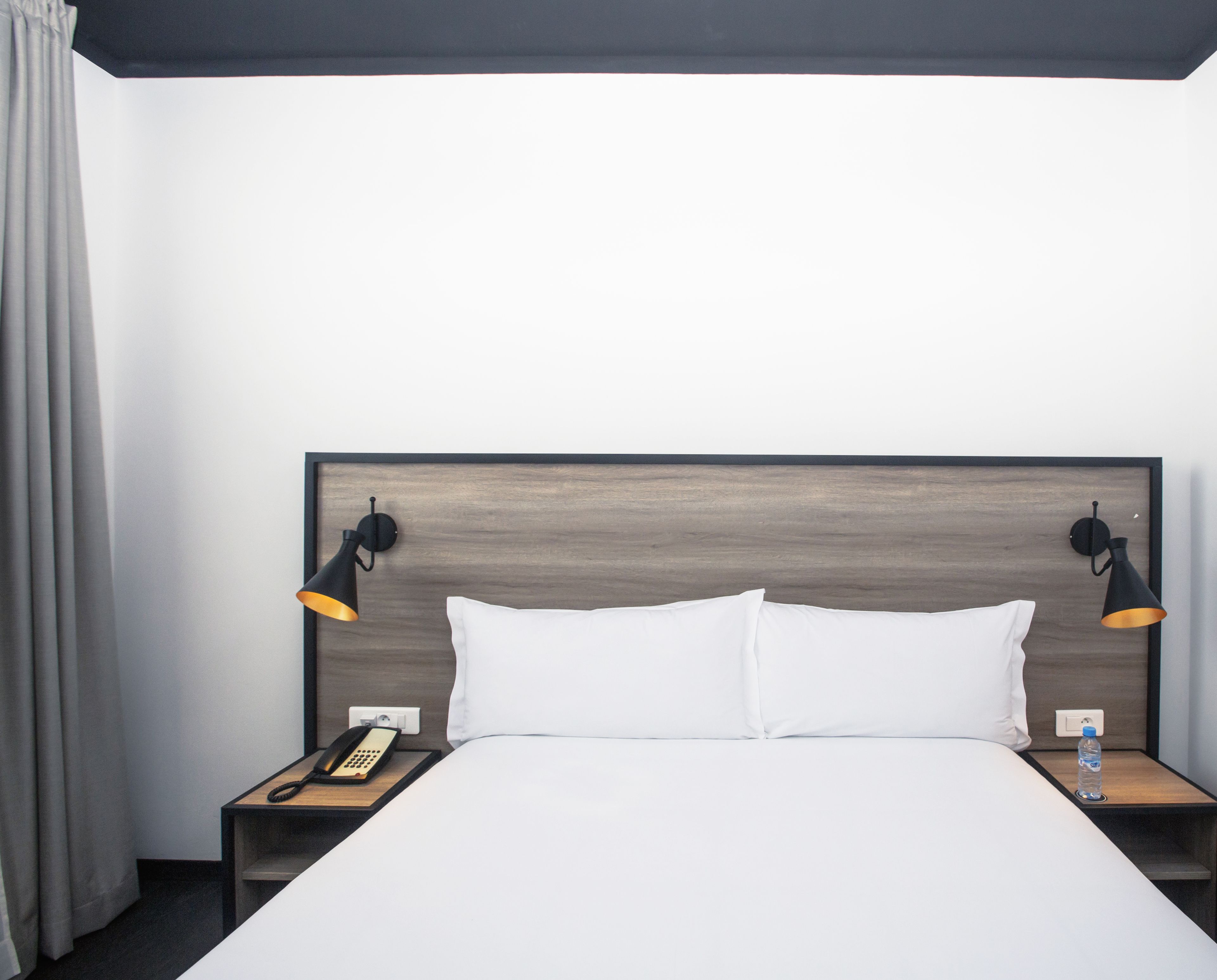 A hotel room with a large bed, two bedside tables, a telephone, and a water bottle.