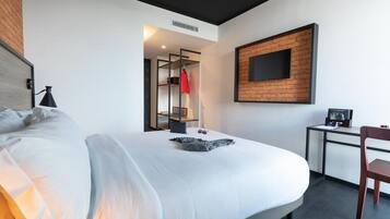 Una habitación de hotel moderna con una cama grande, un escritorio y un televisor montado en una pared de ladrillo.
