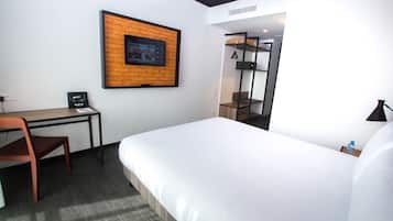 A hotel room with a bed, desk, chair, and a brick-patterned wall.