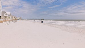 A beach with a pier extending into the ocean, a few people walking along the shore, and buildings on the left side of the beach. - 3 bedroom-2 bathroom Beach house in the heart of Garden City/Murrells Inlet (Murrells Inlet)