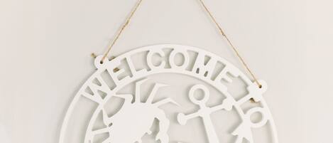 A white circular sign with cut-out letters spelling "WELCOME VISIT" and a silhouette of a person holding an anchor.